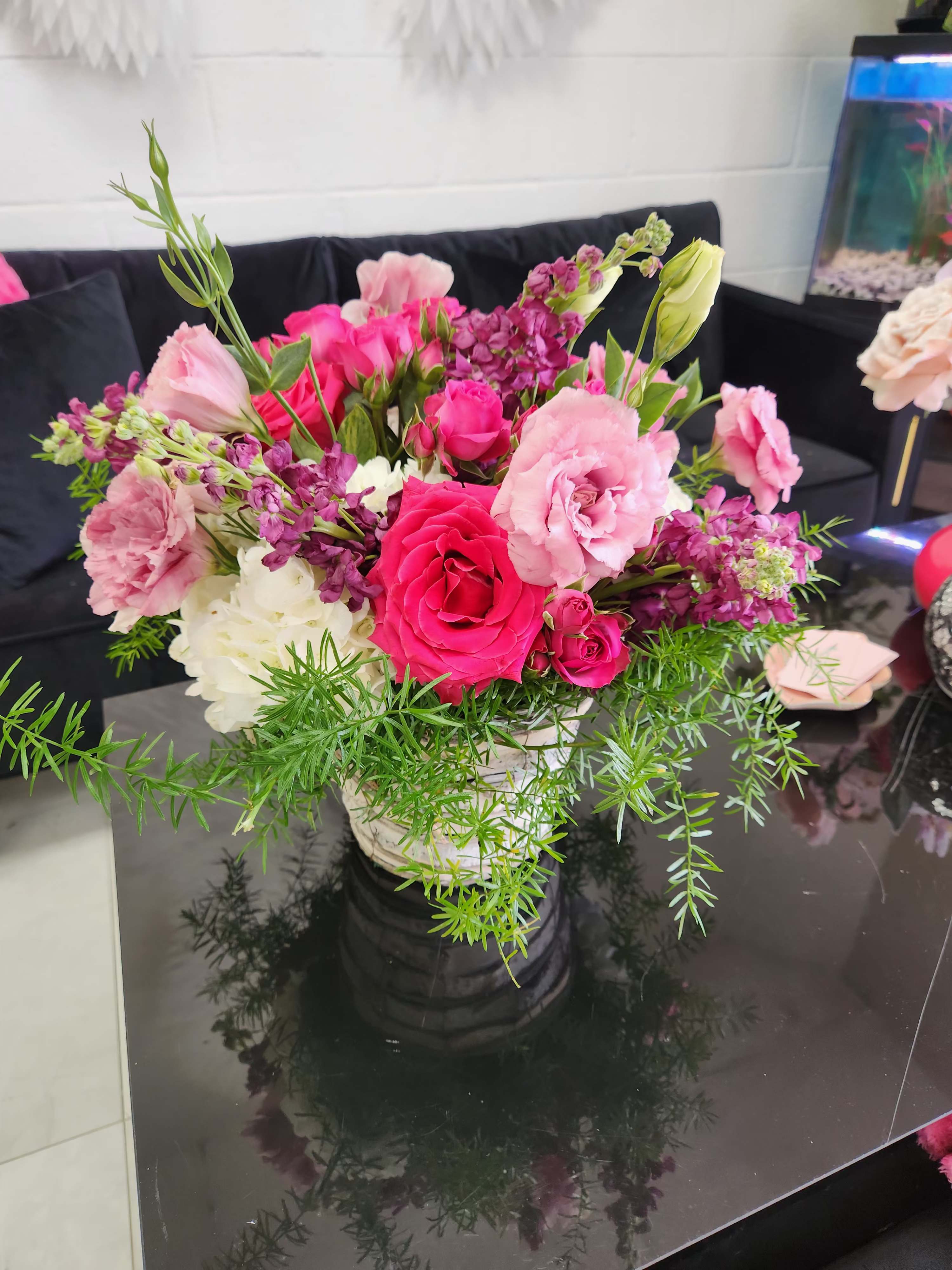 Mixed pink and white flower arrangement with trailing greenery in a white pot on a black table
