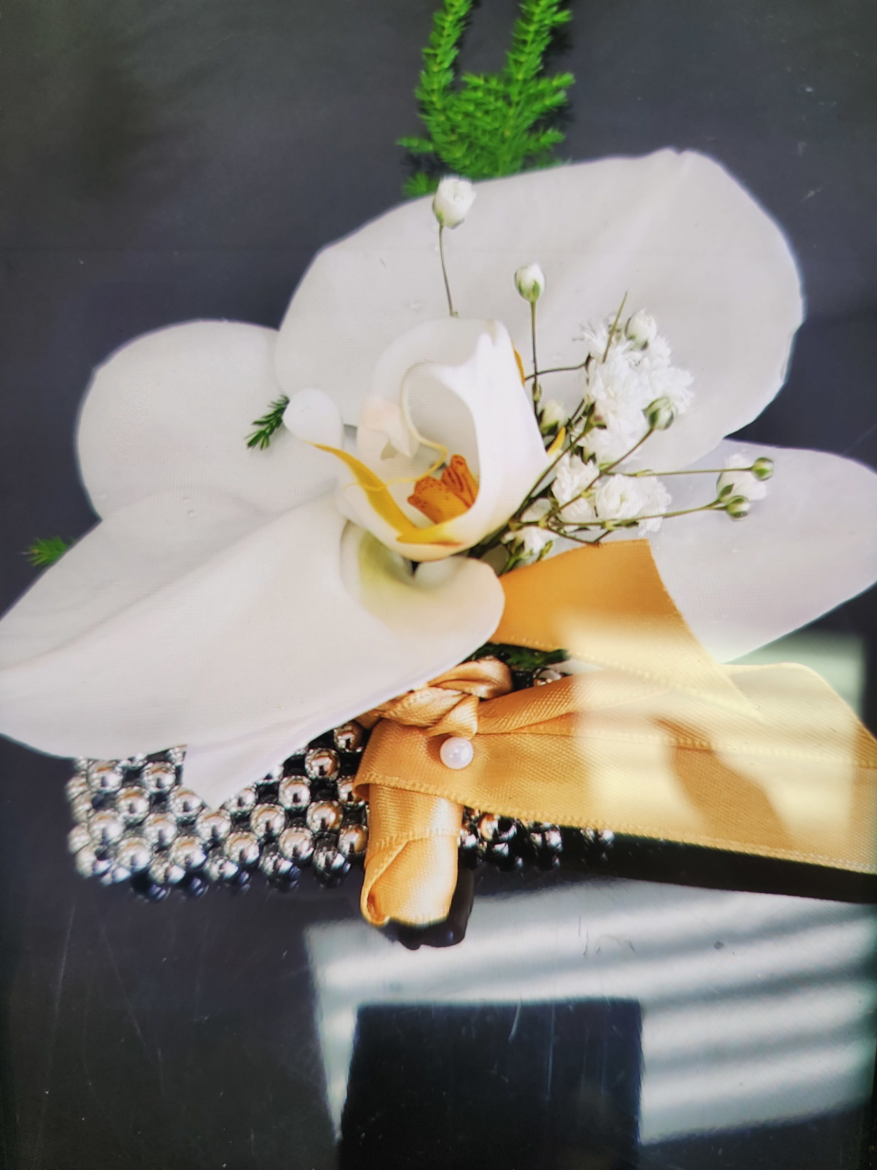White orchid wrist corsage with small white blooms, gold ribbon, and rhinestone bracelet.