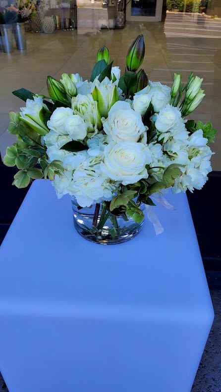 Low glass vase of white roses, lilies, and hydrangeas in a rounded arrangement