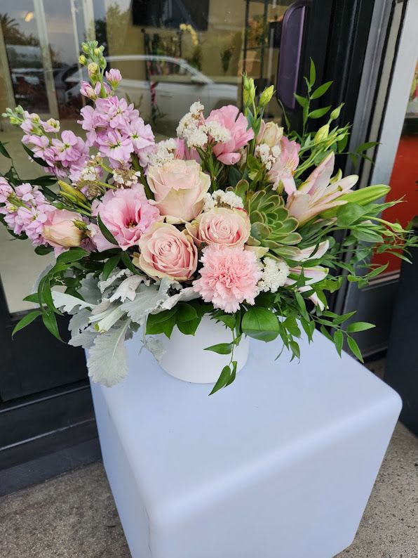 Low arrangement of soft pink roses, carnations, lilies and succulents in a white vase