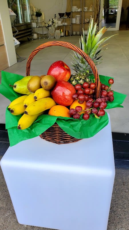 Wicker basket filled with assorted fresh fruit including bananas, apples, grapes, and a pineapple.