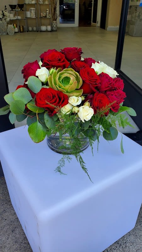 Low round arrangement of red and white roses with a green succulent in a clear glass bowl vase