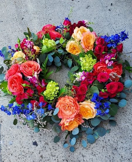 Bright circular wreath of roses, hydrangea, and blue delphinium on a concrete surface