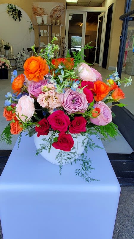 Colorful arrangement of roses and ranunculus in a white bowl-shaped vase