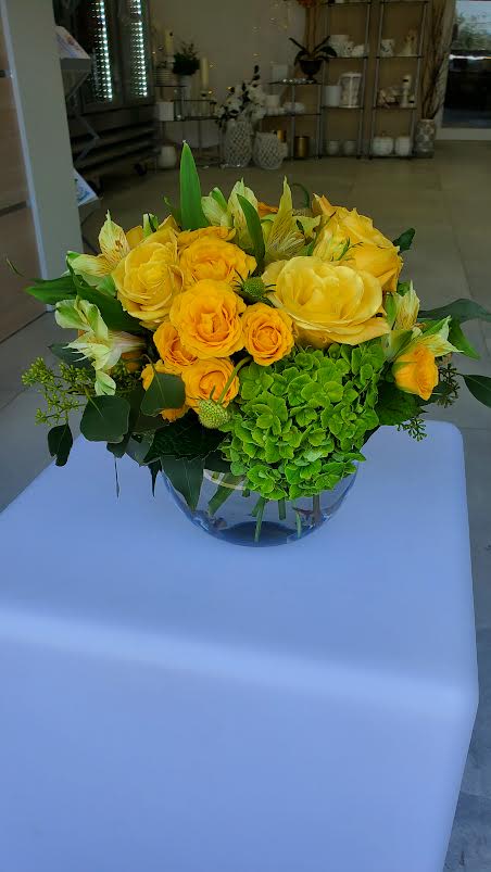 Low arrangement of yellow roses and alstroemeria with green hydrangea in a clear glass bowl vase