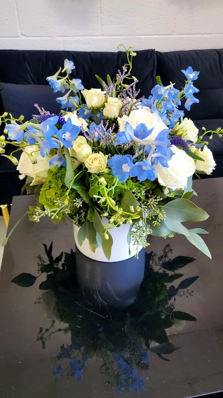 Blue and white flower arrangement with roses and delphinium in a white vase on a black table