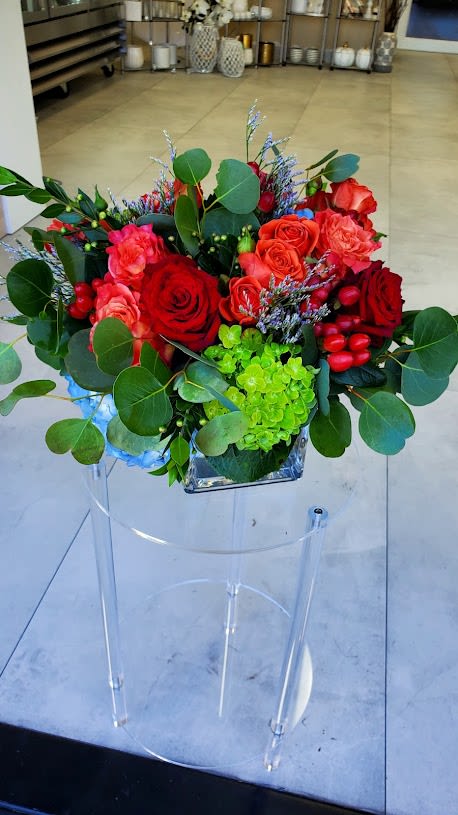 Low arrangement of red and coral roses with green hydrangea in a square glass vase