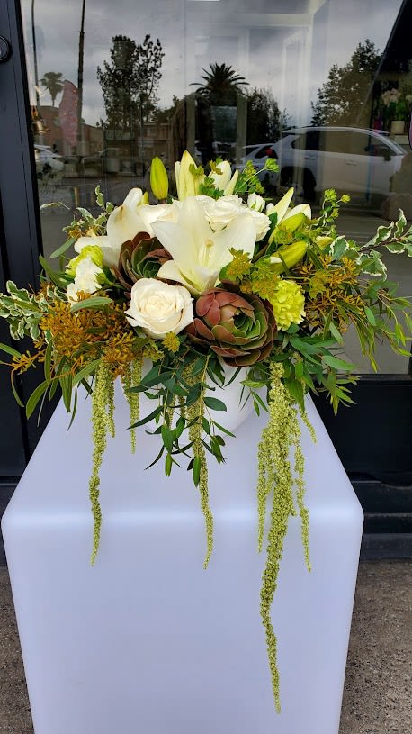 Low white bowl arrangement with white lilies, roses, succulents, and trailing green accents