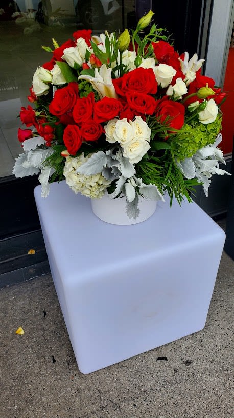 Round arrangement of red and white roses with white lilies in a white vase