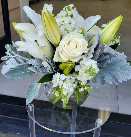 White lilies and a rose with silvery foliage in a round glass vase