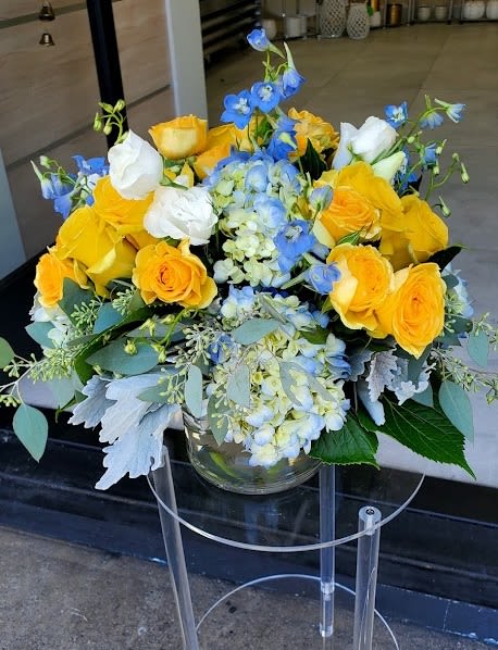 Low glass vase of yellow roses, white blooms, and blue hydrangea and delphinium