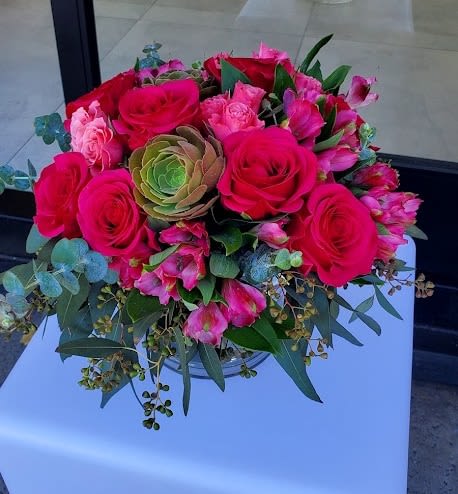 Low arrangement of bright pink roses and alstroemeria with a green succulent in a clear glass vase