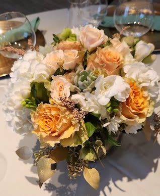 Low centerpiece of peach roses and white flowers in a clear glass vase