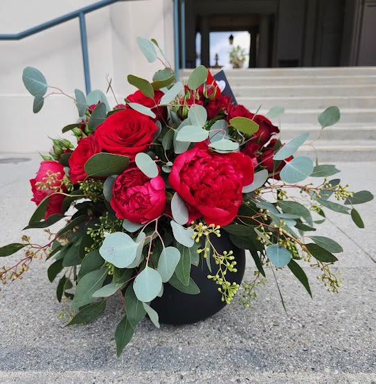 Low arrangement of red roses and peonies with eucalyptus in a round black vase