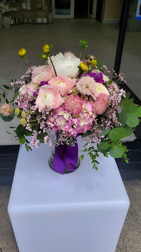 Round arrangement of pink and white mixed flowers in a glass vase with a purple ribbon