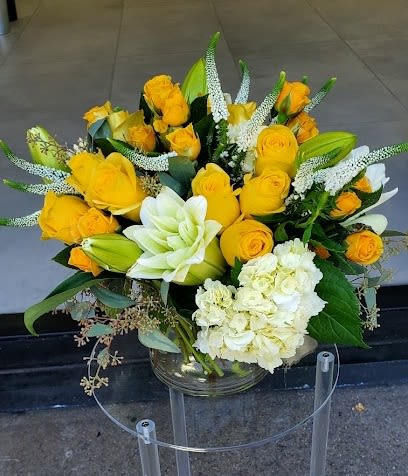 Yellow rose and white lily arrangement with white hydrangeas in a clear glass vase