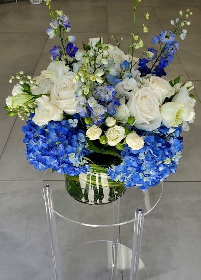 Low arrangement of white roses and blue hydrangeas in a clear glass vase.