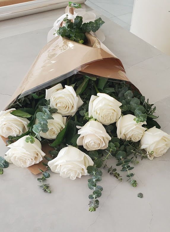 Bouquet of long-stem white roses with eucalyptus wrapped in tan paper and cellophane