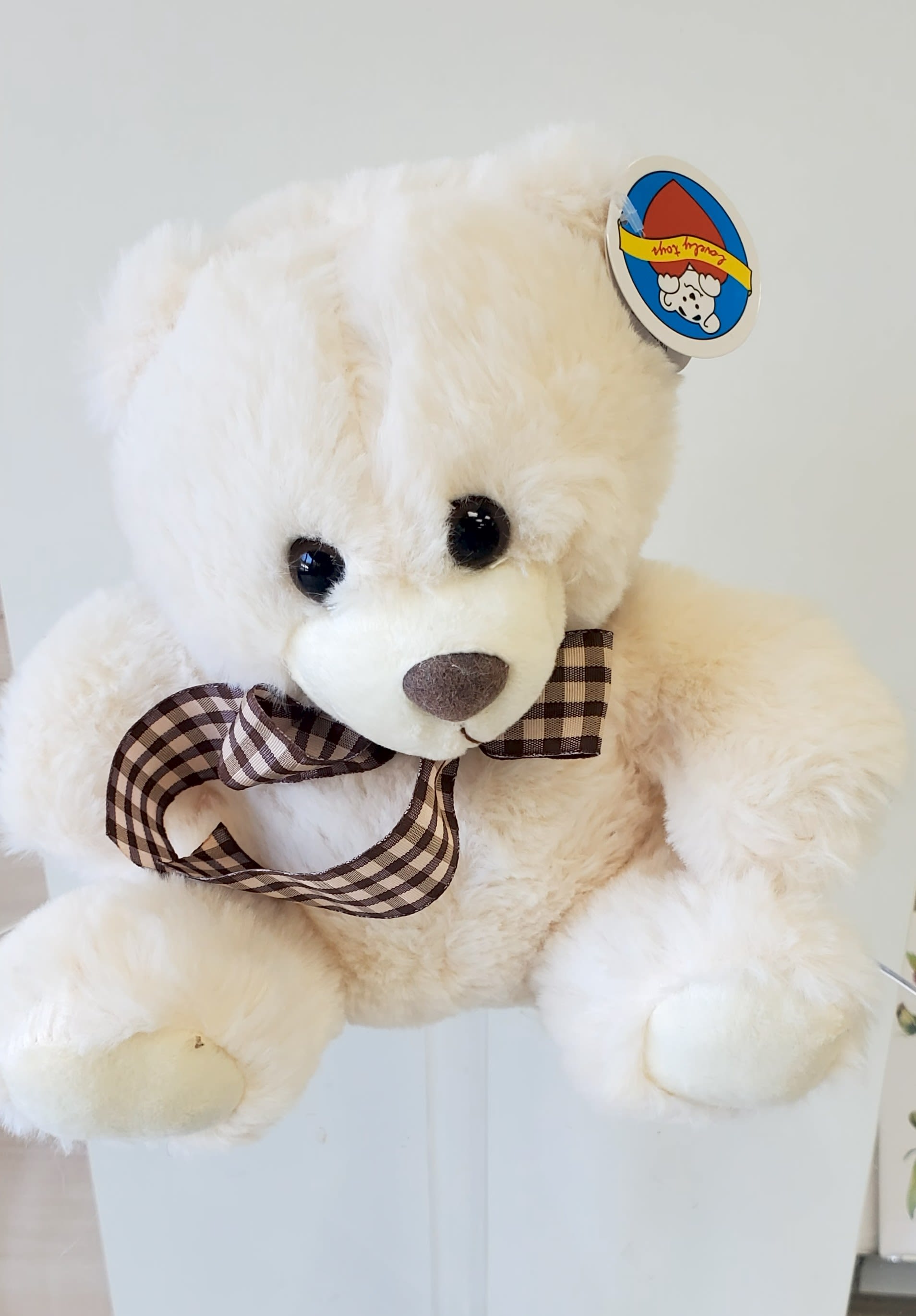 Cream plush teddy bear with a checked brown bow sitting against a light background