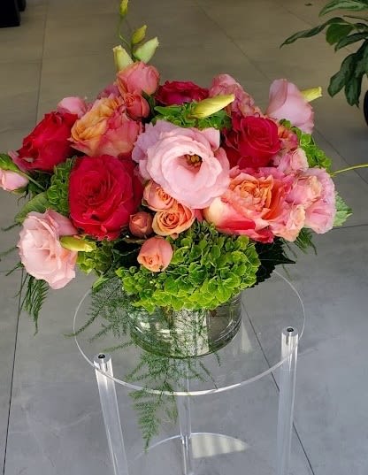 Round arrangement of pink and red roses and lisianthus with green hydrangea in a glass vase