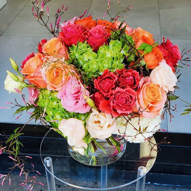 Bright bouquet of orange, pink, and cream roses with green hydrangeas in a clear glass vase
