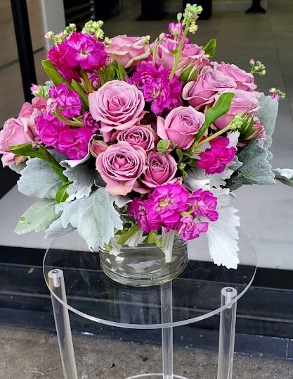 Compact arrangement of light pink roses and bright fuchsia blooms in a clear glass vase with silvery foliage