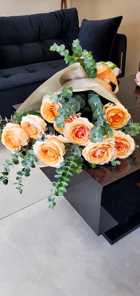 Bouquet of peach roses with eucalyptus in beige wrap resting on a black table