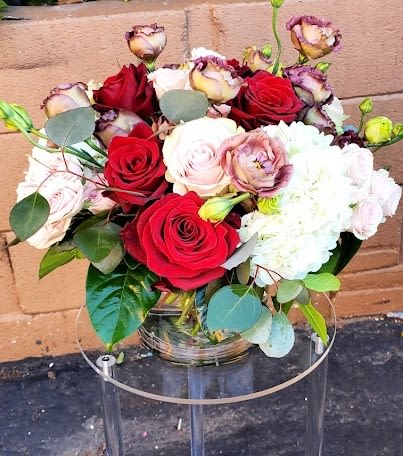 Low round arrangement of red and blush roses with white blooms in a clear glass vase