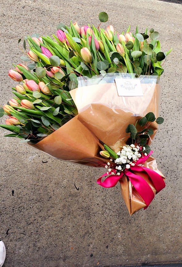 Large bouquet of pink and peach tulips wrapped in brown paper with a bright pink ribbon
