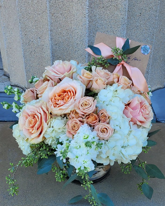 Low arrangement of peach roses and white hydrangeas in a glass vase with a card tied by a ribbon