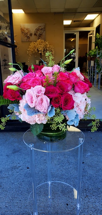 Low round arrangement of hot pink and light pink roses in a glass vase on a clear stand