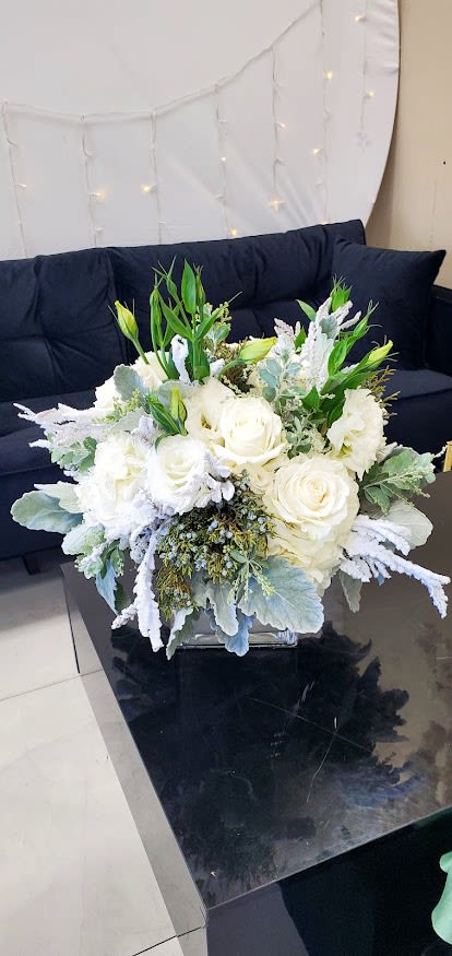 Low white rose and lisianthus arrangement in a clear glass cube vase.