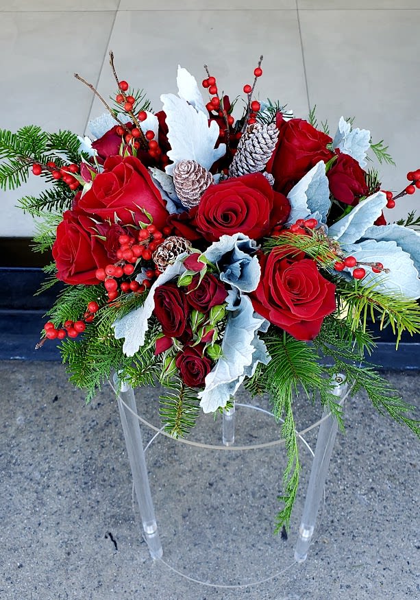 Low centerpiece of red roses with red berries, frosted pinecones, and evergreens in a winter arrangement