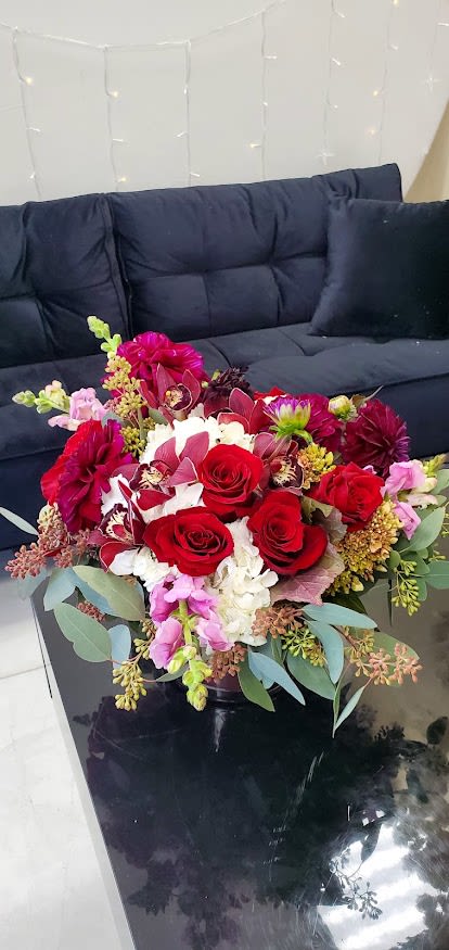 Low arrangement of red roses, orchids, and white hydrangeas in a black vase on a coffee table