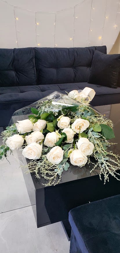Hand-tied bouquet of white roses wrapped in clear cellophane on a black table