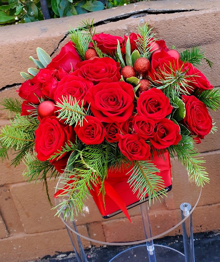 Arrangement of red roses with evergreen sprigs in a red square container