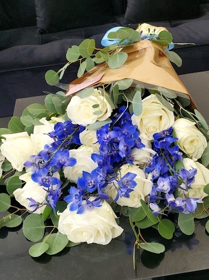 Bouquet of white roses and bright blue orchids wrapped in gold paper
