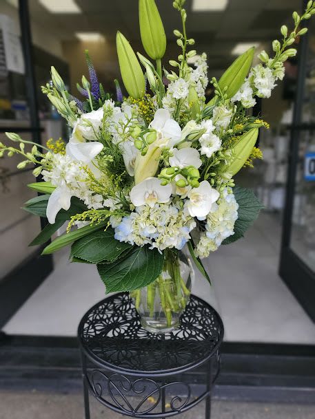 Stand white - Full, upright mix of white lilies, orchids and hydrangea-like blooms with green stems in a clear vase.