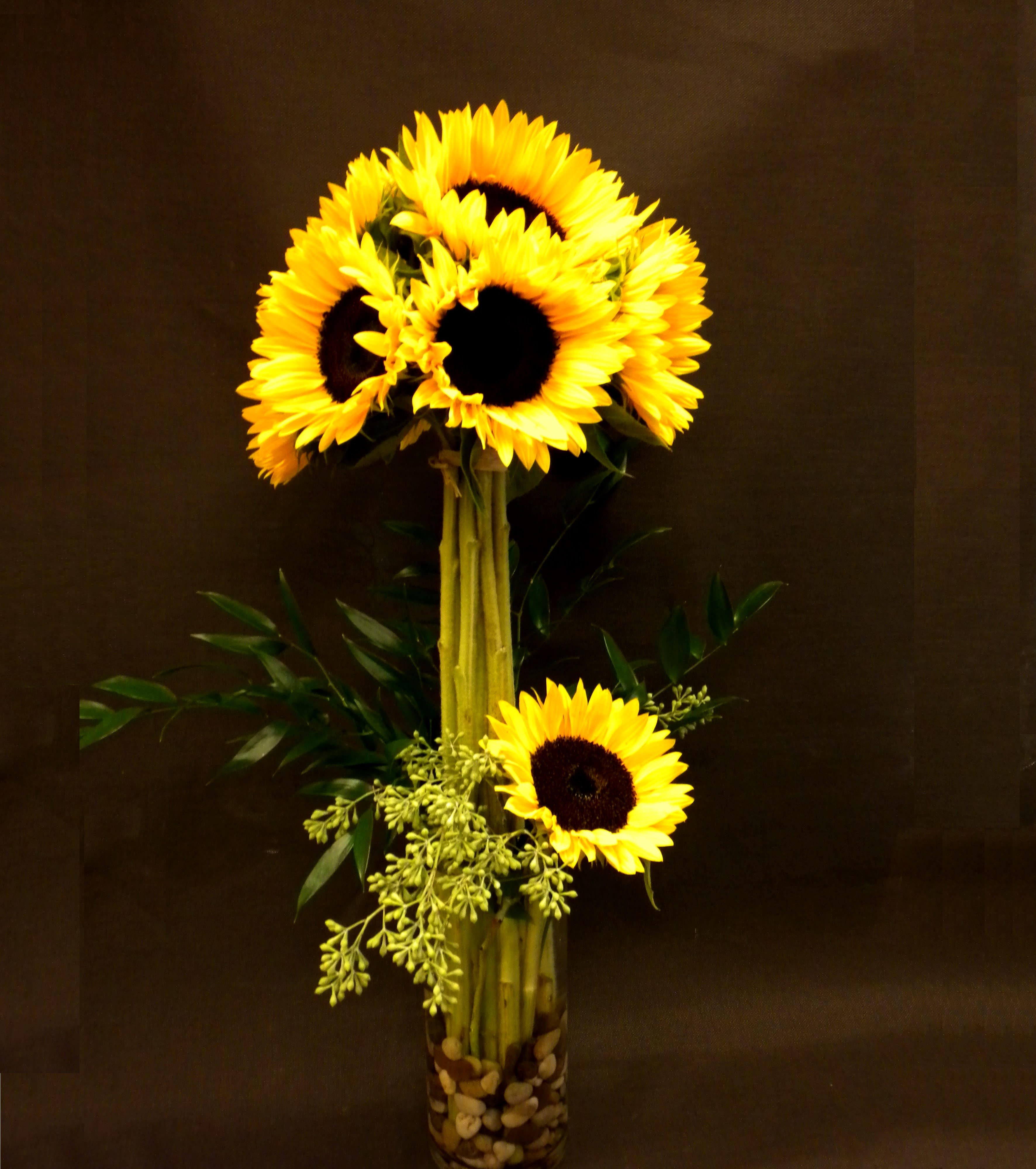 Tall sunflower arrangement in a glass vase with decorative stones