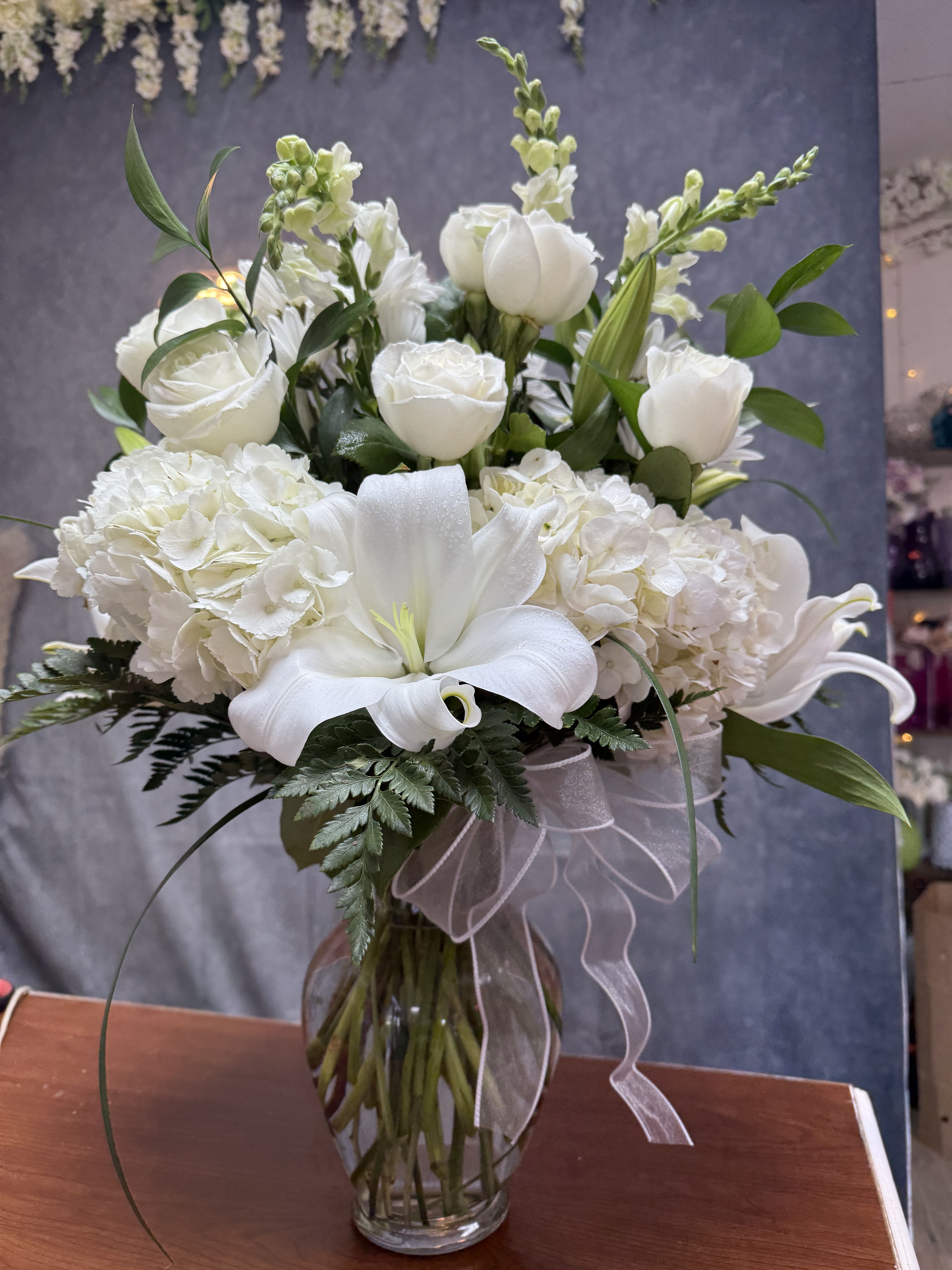 White lilies, roses, and hydrangeas in a glass vase with a sheer ribbon