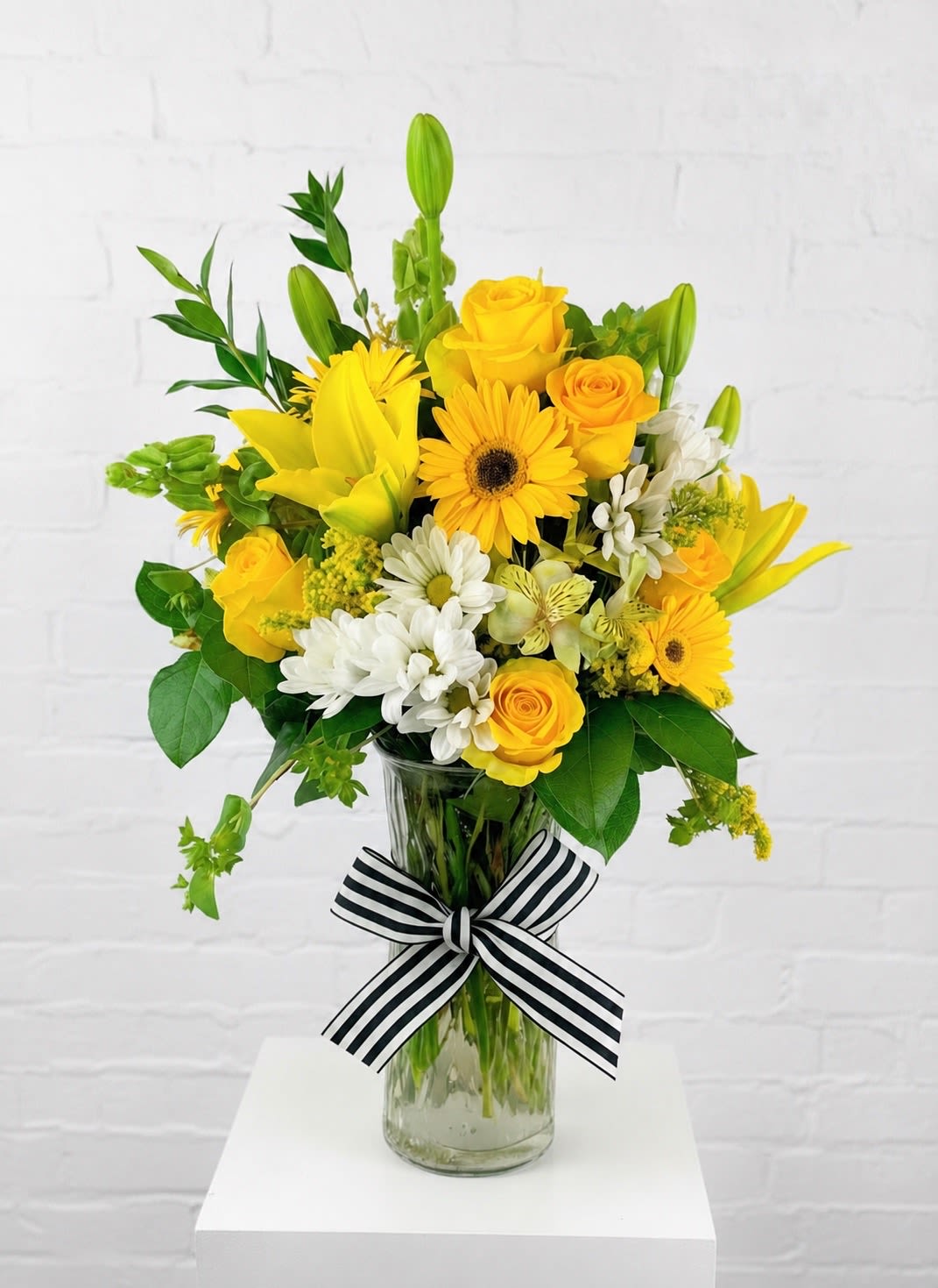 Yellow and white mixed bouquet in a glass vase with a striped ribbon