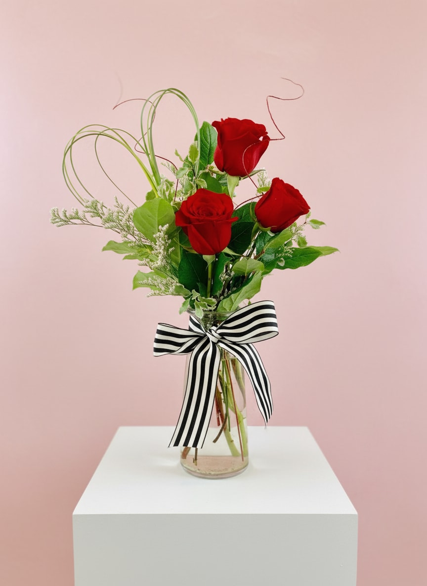 Three red roses in a glass vase with a black-and-white striped bow