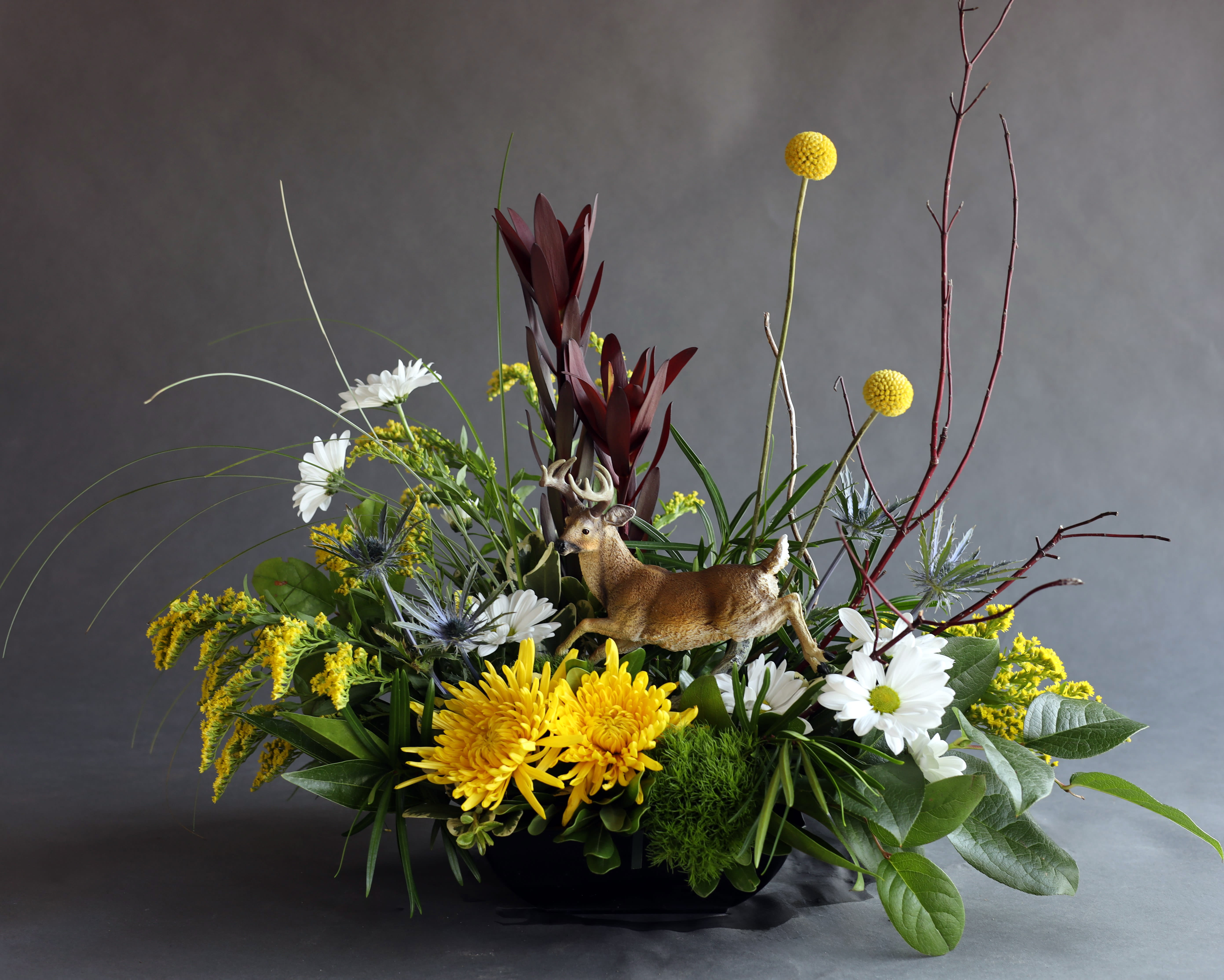 Mixed floral arrangement with a deer figurine in a low black container