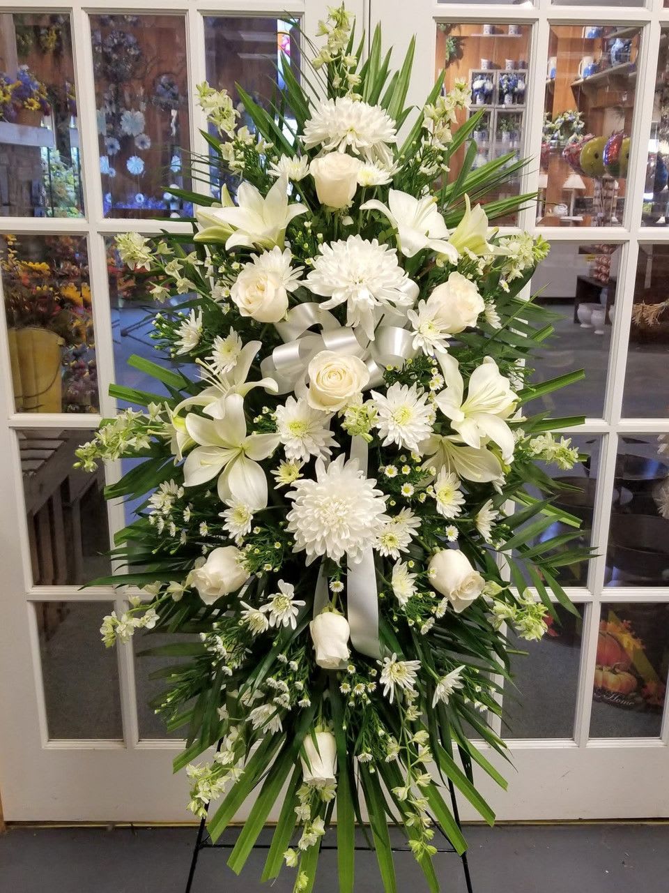 Large white funeral spray with lilies, roses, and chrysanthemums on an easel