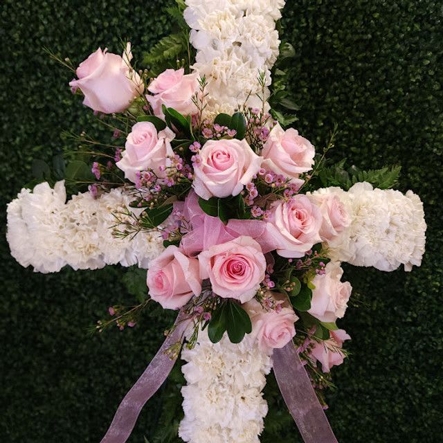 Pink roses and white flowers arranged on a cross with a lavender ribbon