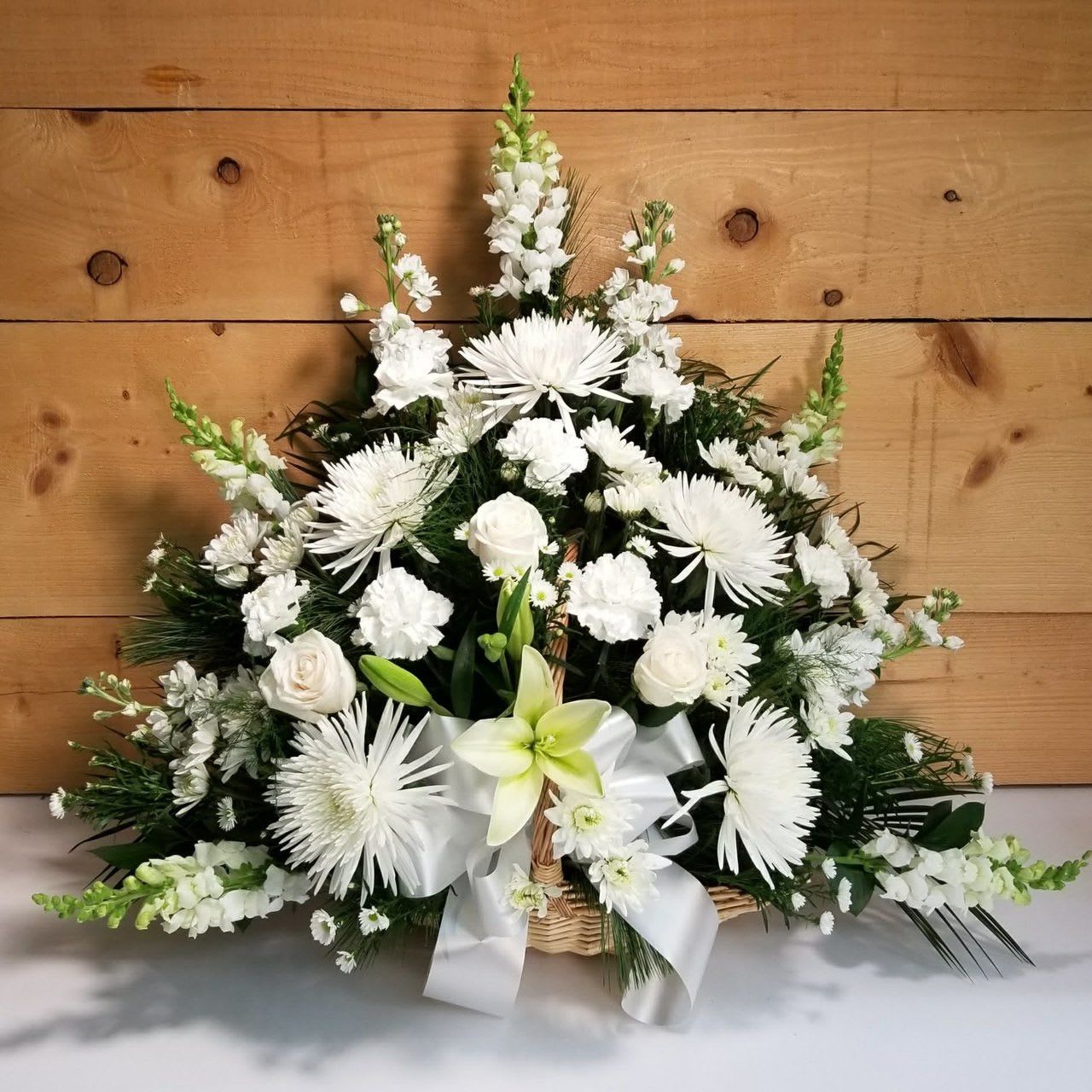 White floral arrangement in a wicker basket with a white ribbon
