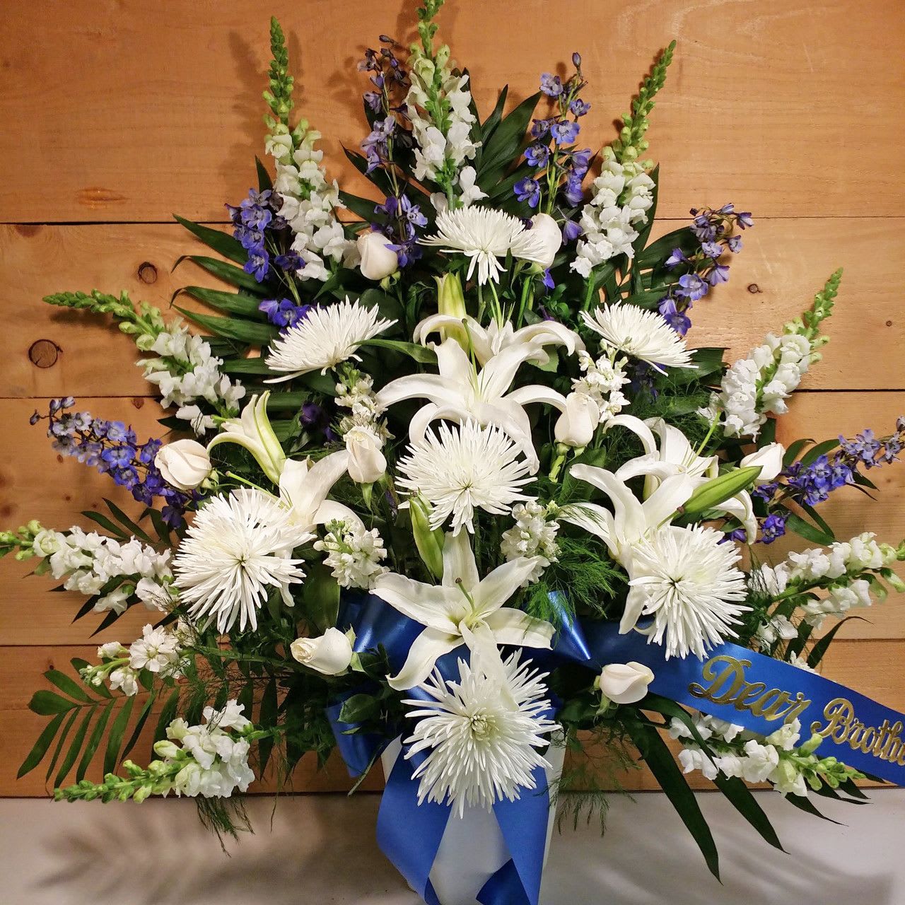 White lilies and chrysanthemums with blue ribbon on a sympathy spray