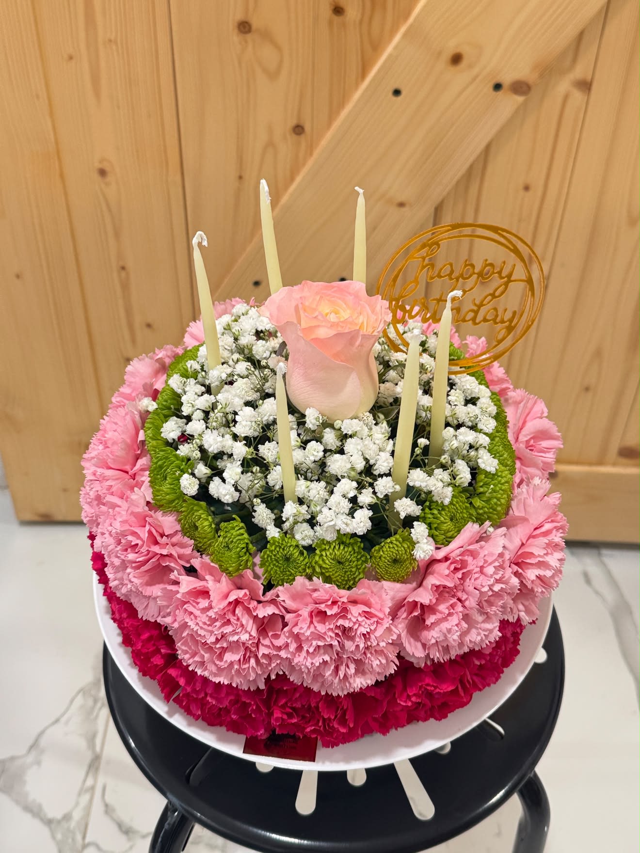 Floral Cake Arrangement – A Sweet Surprise That Lasts - Celebrate life’s special moments with our beautiful Floral Cake Arrangement, handcrafted with fresh carnations and topped with an elegant  rose. Designed to resemble a real cake, this unique floral creation is the perfect gift for birthdays and other memorable occasions.  Complete with decorative candles and a “Happy Birthday” topper, it’s ready to impress from the moment it arrives. Each arrangement is carefully handcrafted using premium fresh flowers to create a stunning and unforgettable gift.  Local delivery available throughout Miami.
