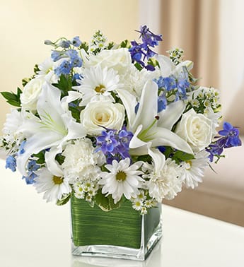 Healing Tears - Blue and White - Product ID: 100231  Send your deepest care and concern during times of sorrow with our precious blue and white sympathy arrangement. The freshest roses, delphinium, lilies, daisy poms and carnations are hand-designed in a stunning cube vase as a gesture of comfort and peace. Elegant blue and white arrangement of roses, delphinium, lilies, daisy poms, carnations and monte casino, accented with variegated pittosporum and myrtle Artistically designed by our florists in a classic clear glass cube vase lined with a Ti leaf ribbon; vase measures 5"H x 5"D Appropriate for the service or for sending to the home or office of friends and family members Large arrangement measures approximately 11"H x 11"L Medium arrangement measures approximately 10"H x 10"L Small arrangement does not include roses and measures approximately 9"H x 9"L Our florists hand-design each arrangement, so colors, varieties, and container may vary due to local availability Lilies may arrive in bud form and will open to full beauty over the next 2-3 days