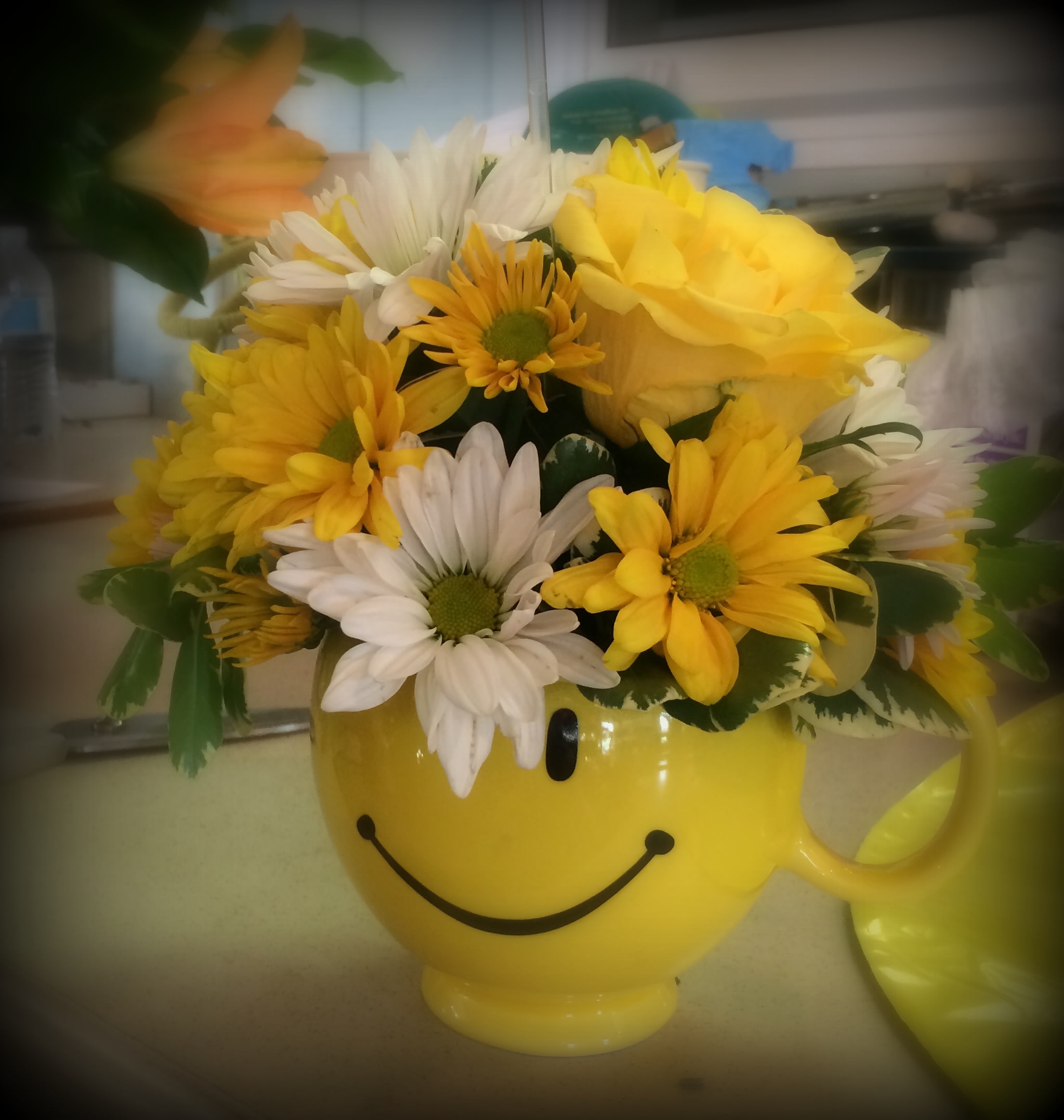 Yellow smiley-face mug filled with yellow and white daisies